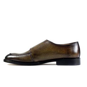 May include: A brown leather monk strap shoe with a textured finish. The shoe has a black sole and a buckle closure.