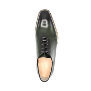 May include: A green leather oxford shoe with a lace-up closure. The shoe has a brown leather sole and a polished finish.