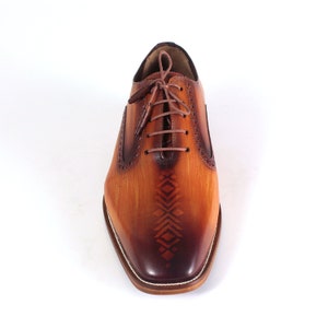 May include: A pair of brown leather oxfords with a geometric pattern on the toe. The shoes have a lace-up closure and a rounded toe.