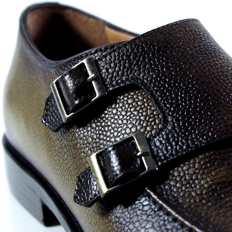 May include: A pair of brown leather dress shoes with double buckles. The shoes have a textured leather upper and a black leather strap with silver buckles.