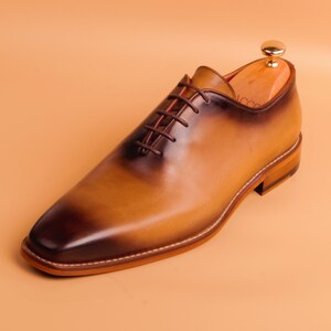 May include: A brown leather lace-up oxford shoe with a burnished finish. The shoe has a rounded toe and a low heel.