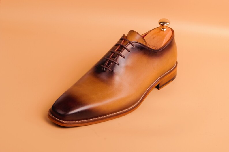 May include: A brown leather lace-up oxford shoe with a burnished finish. The shoe has a rounded toe and a low heel.
