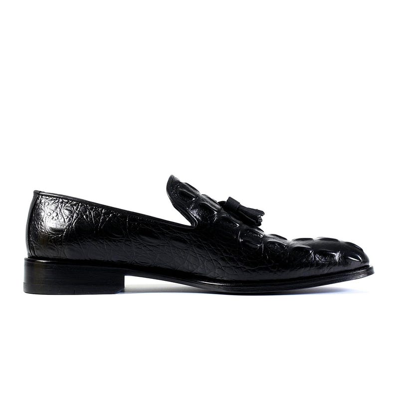 K&ouml;nnte beinhalten: Schwarzer Lederloafer mit strukturiertem, krokodil&auml;hnlichem Muster. Der Schuh hat ein kleines Quastendetail und einen niedrigen Absatz. Das gl&auml;nzende Finish verleiht diesem klassischen Schuhdesign einen Hauch von Eleganz.