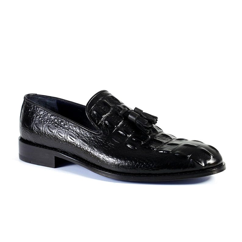K&ouml;nnte beinhalten: Schwarzer Lederloafer mit Krokodiltextur und kleinem Quastendetail. Der Schuh hat einen niedrigen Absatz und eine runde Spitze. Ein klassischer Schuhstil.