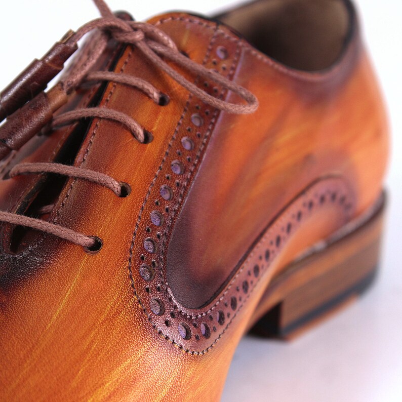 May include: Close-up of a brown leather oxford shoe with a brogue design. The shoe has a lace-up closure and a brown leather sole.