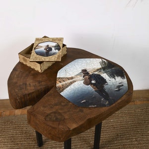 Op de afbeelding: Een houten legpuzzel met een foto van een persoon met een hoed die in een rivier staat. De puzzel is gedeeltelijk in elkaar gezet op een houten tafel. Een bijpassende houten doos met een ingelijste foto is ook aanwezig.