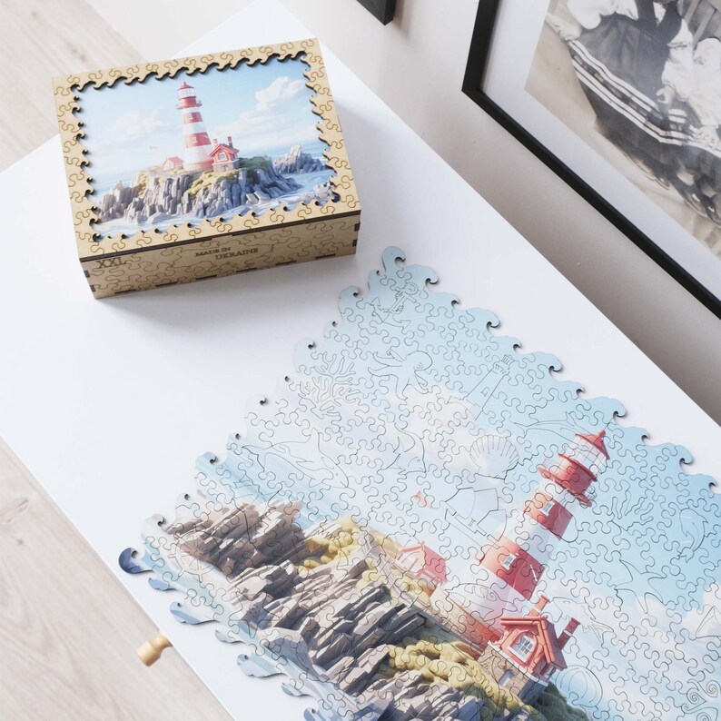 May include: A completed jigsaw puzzle of a lighthouse on a rocky coastline. The puzzle is made of blue and white pieces and features a red and white lighthouse with a blue sky and ocean in the background.