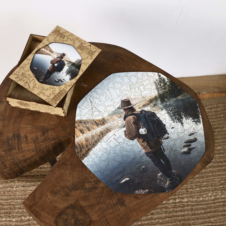 Op de afbeelding: Houten legpuzzel met een afbeelding van een persoon bij een meer. De puzzel is gedeeltelijk in elkaar gezet, met stukjes op een houten oppervlak. Een houten doos met een bijpassende afbeelding is ook aanwezig.