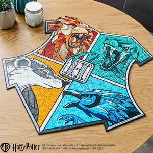 May include: A colorful jigsaw puzzle featuring the Hogwarts crest, with sections depicting a lion, snake, badger, and eagle. The puzzle is on a wooden surface. The Harry Potter logo is visible at the bottom.
