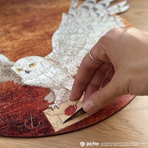 Könnte beinhalten: Ein Holzpuzzle mit einem Schneeeulen-Motiv, die im Flug zu sehen ist. Auf dem Boden liegt ein Briefumschlag mit einem roten Wachssiegel. Das Puzzle ist teilweise zusammengesetzt.