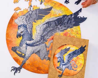 May include: A wooden jigsaw puzzle featuring a griffin with gray and blue feathers against an orange and yellow background. The puzzle is partially assembled, with some pieces scattered around. A box with the griffin image is also present.
