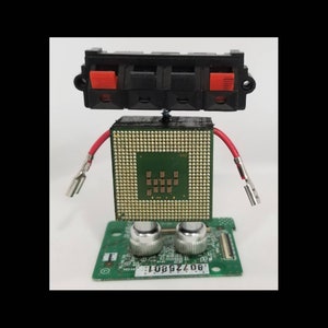 May include: A robot sculpture made from electronic components. The head is a black connector with red accents, the body is a green CPU, and the arms are red wires. The robot is mounted on a green circuit board.