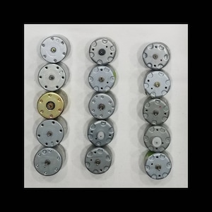 May include: A collection of small, silver-colored DC electric motors arranged in three columns. Each motor has a circular design with various screw placements and a central shaft. One motor has a gold-colored casing.