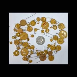 May include: A collection of small, yellow electronic components with wire leads, scattered on a white surface. A US quarter coin is included for size reference. The components vary in size and shape, with some having red markings.