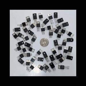 May include: A collection of black electronic components with silver pins, arranged in a circular pattern. A quarter coin is in the center. The components have various markings and are on a white surface.