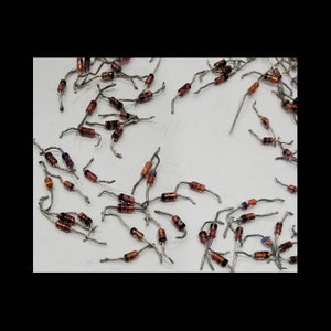 May include: A collection of small electronic diodes with red, black, and blue bands. The diodes have silver-colored wire leads and are scattered across a white surface. These components are used in various electronic circuits.