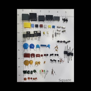 May include: A collection of electronic components, including capacitors, resistors, and transistors, arranged on a white surface. Components vary in size, shape, and color, with a ruler for scale. The word "Square" is visible.