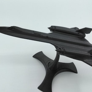 Puede incluir: Un modelo de avión negro de un SR-71 Blackbird sobre una base negra. El modelo está detallado con las características distintivas del SR-71, incluidas las alas en flecha y los dos motores.