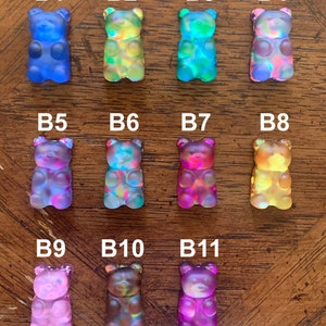 May include: An assortment of eleven colorful gummy bear figurines. Each bear is a different color, including blue, green, pink, and yellow. The bears are arranged in three rows, with the letters B1 through B11 above each bear.