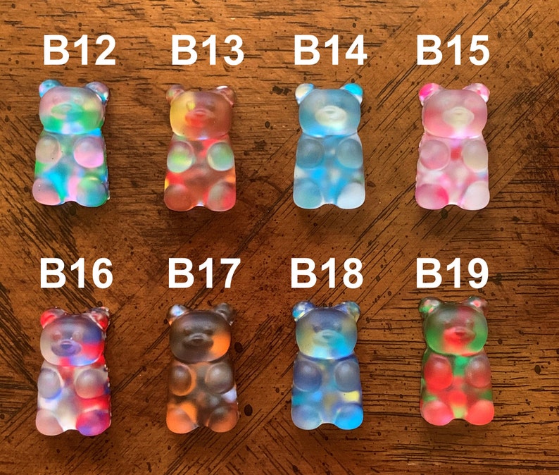May include: A collection of eight colorful gummy bear figurines. Each bear is a different color, including blue, pink, red, and green. The bears are labeled with the letters "B" followed by a number.
