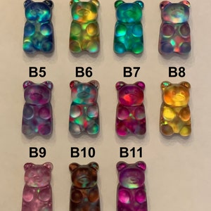 May include: A collection of eleven iridescent gummy bear charms in various colors. The bears have a glossy finish and are arranged in three rows. Colors include blue, green, yellow, purple, and brown. Each bear is labeled with a "B" followed by a number.