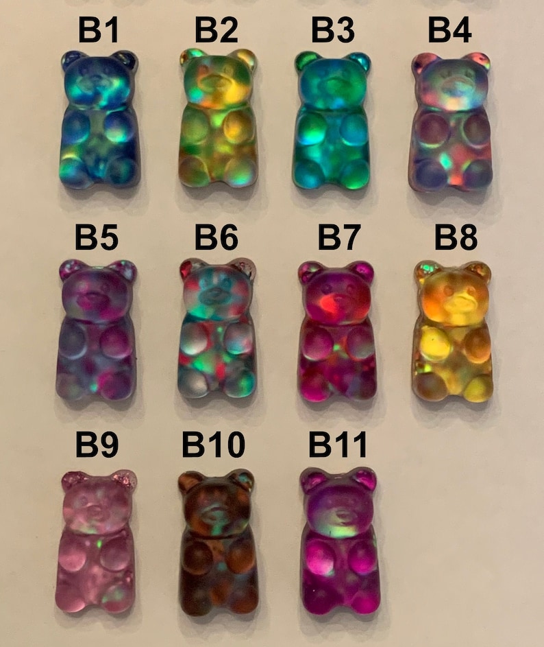May include: A collection of eleven iridescent gummy bear charms in various colors. The bears have a glossy finish and are arranged in three rows. Colors include blue, green, yellow, purple, and brown. Each bear is labeled with a "B" followed by a number.