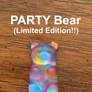 May include: A colorful gummy bear figurine with a rainbow hue. The text "PARTY Bear (Limited Edition!!)" is displayed above the bear. The bear is translucent and has a frosted appearance, with visible details.