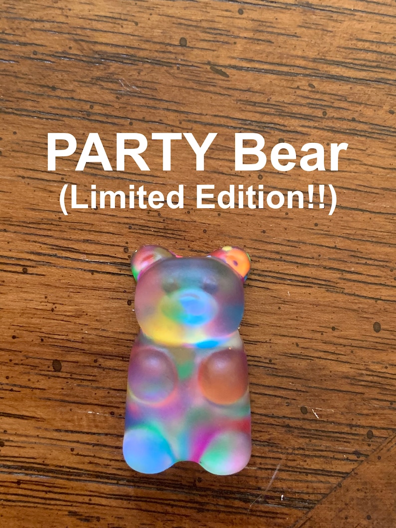 May include: A colorful gummy bear figurine with a rainbow hue. The text "PARTY Bear (Limited Edition!!)" is displayed above the bear. The bear is translucent and has a frosted appearance, with visible details.