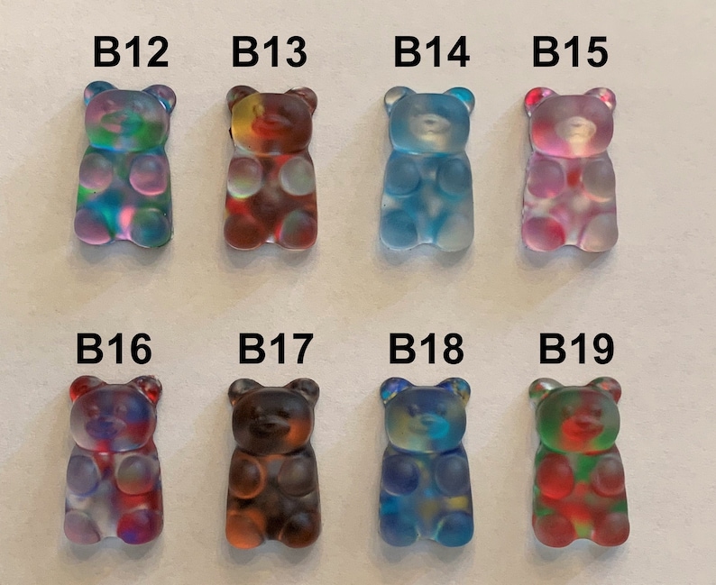 May include: Eight colorful gummy bear-shaped resin charms. Each charm is a different color, including blue, green, red, and purple. The charms are labeled B12 through B19. These charms are ideal for jewelry making or other craft projects.