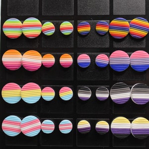May include: A display of 10 pairs of round, colorful, striped earrings. Each pair features a different pride flag design, including rainbow, bisexual, transgender, non-binary, and asexual.