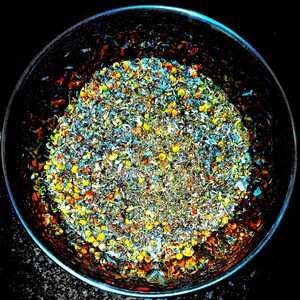 May include: A close-up of a metal bowl filled with a mixture of dried herbs and flowers. The herbs and flowers are a variety of colors, including yellow, orange, red, and green.