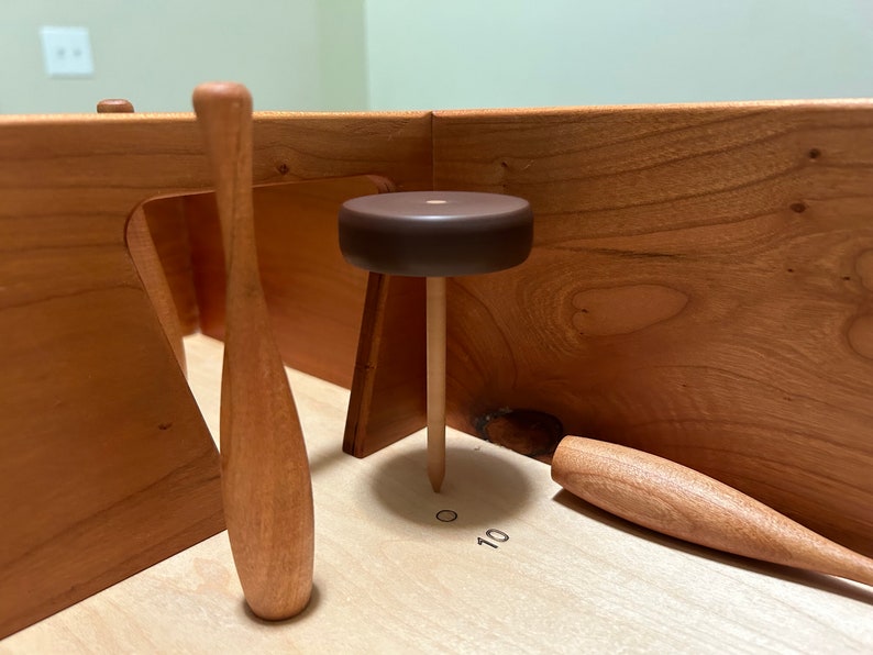 May include: A wooden game with three wooden bowling pins and a brown wooden ball. The game has a number 10 printed on the surface.