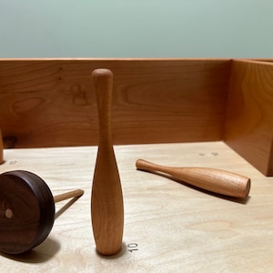 May include: A wooden game set with a brown wooden wheel and several wooden bowling pins. The pins are arranged on a light wood surface with numbers marked on the surface.