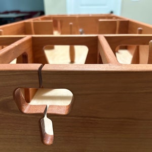 May include: Close-up of a wooden game board with a cutout in the shape of a T. The board is made of light brown wood and has a natural finish.