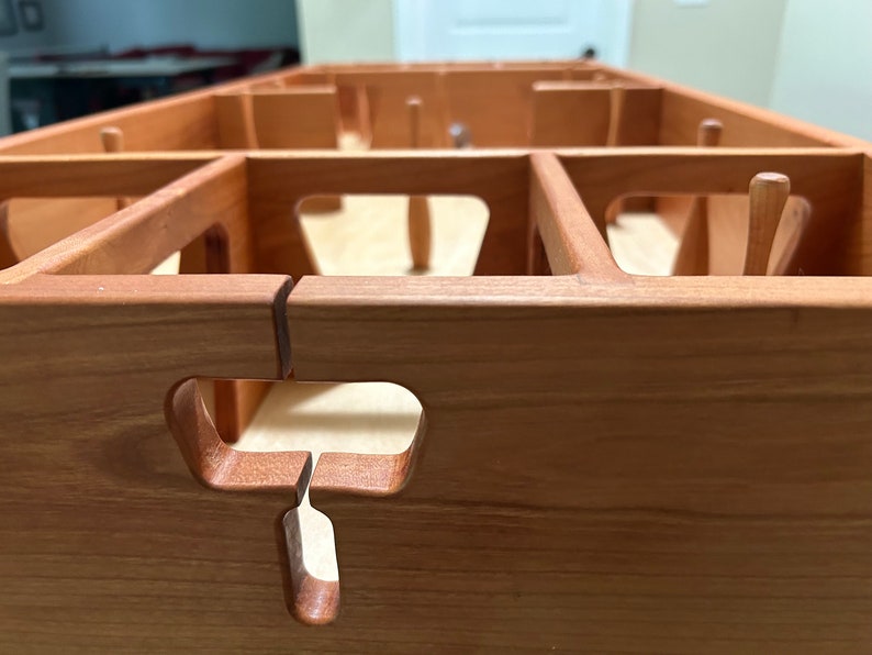 May include: Close-up of a wooden game board with a cutout in the shape of a T. The board is made of light brown wood and has a natural finish.