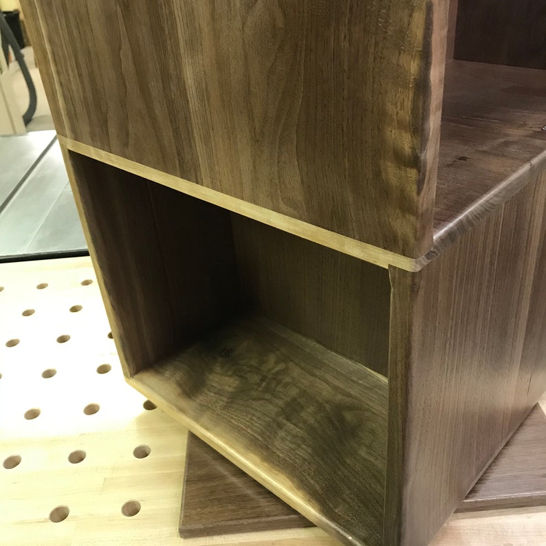 以下が含まれることがあります： 濃い茶色の仕上げのウッドシェルフユニット。棚はオープンシェルフが1つあり、無垢材で作られています。