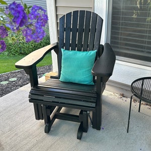 Op de afbeelding: Zwarte houten glijstoel met een turquoise kussen op een betonnen terras.