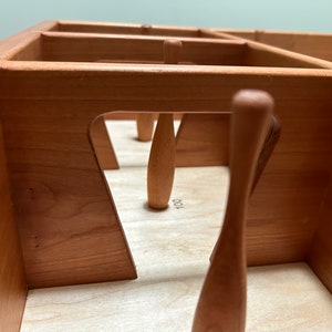 May include: A wooden tabletop game with a set of wooden bowling pins. The pins are arranged in a triangular formation. The game is made of natural wood and has a light brown finish.