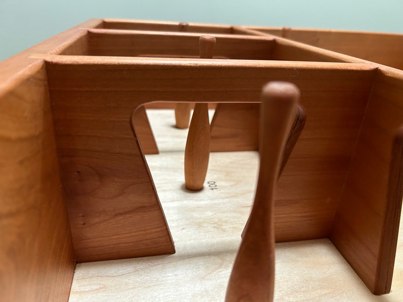 May include: A wooden tabletop game with a set of wooden bowling pins. The pins are arranged in a triangular formation. The game is made of natural wood and has a light brown finish.