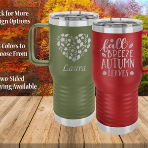 May include: Two stainless steel travel mugs with fall-themed designs. The green mug has a floral heart design and the text "Laura". The red mug has the text "fall breeze autumn leaves".