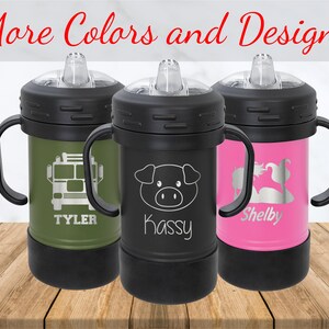 May include: Three insulated sippy cups in olive green, black, and pink. Each cup has a black lid, handles, and base. The olive green cup features a fire truck graphic and the name "Tyler." The black cup has a pig graphic and the name "Kassy." The pink cup has a swan graphic and the name "Shelby."