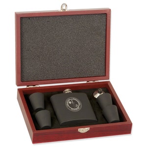 May include: A black metal flask with a silver lid and a silver funnel in a red wooden box with a black foam interior. The flask has a silver inscription on the front. The box includes two black metal shot glasses.