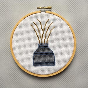 May include: A cross-stitch embroidery hoop with a blue and white vase with yellow stems inside.