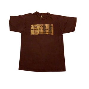 Puede incluir: Una camiseta marr&oacute;n con un estampado rectangular que dice "I don't care too much for money..." con un s&iacute;mbolo de copyright y el texto "New Line Cinema and A Lot of  " debajo del gr&aacute;fico.