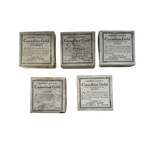 May include: Five small white boxes with black text that reads "Herbert Plant's Canadian Gold for China Decorating Fluxed". Each box contains a piece of gold for decorating china. The boxes are arranged in a grid pattern.