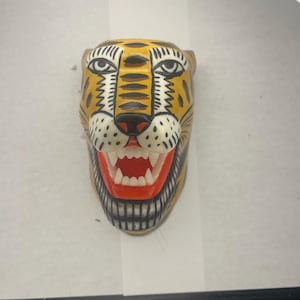 May include: A yellow, black, and white ceramic jaguar head with an open mouth and red teeth. The jaguar has a black and white patterned design on its face.