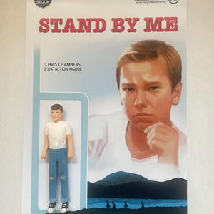 May include: A 3 3/4 inch action figure of Chris Chambers from the movie Stand By Me. The figure is wearing a white t-shirt, blue jeans, and black sneakers. The figure is posed with his hands on his hips. The background of the card is blue with a silhouette of the four boys from the movie walking along a path.