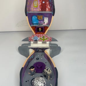 May include: A gray plastic toy head with a removable top, revealing a multi-colored interior with a small figure and a silver foil ball. The head is open and the interior is visible. The toy is a playset with a small figure and a silver foil ball.