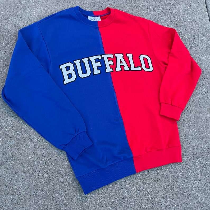 May include: A blue and red sweatshirt with the word "BUFFALO" in white letters on the front.