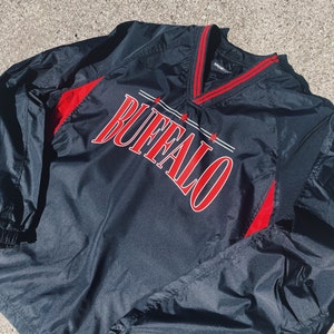 May include: Black windbreaker jacket with red accents and the word "BUFFALO" in red lettering on the front. The jacket has a v-neck and a drawstring hood.